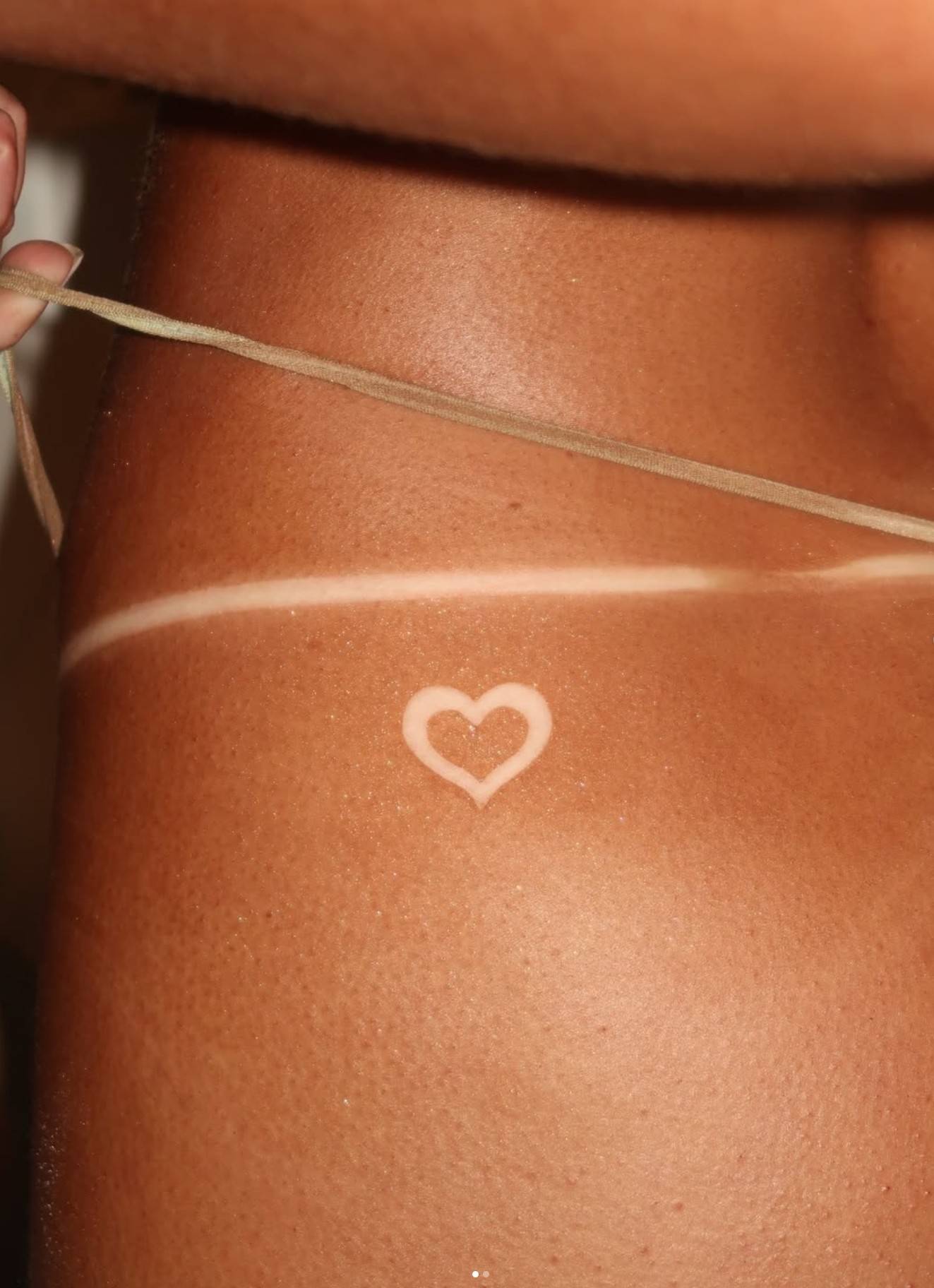a close-up of a tanned back with a heart left in tan-line art and fine string tan lines